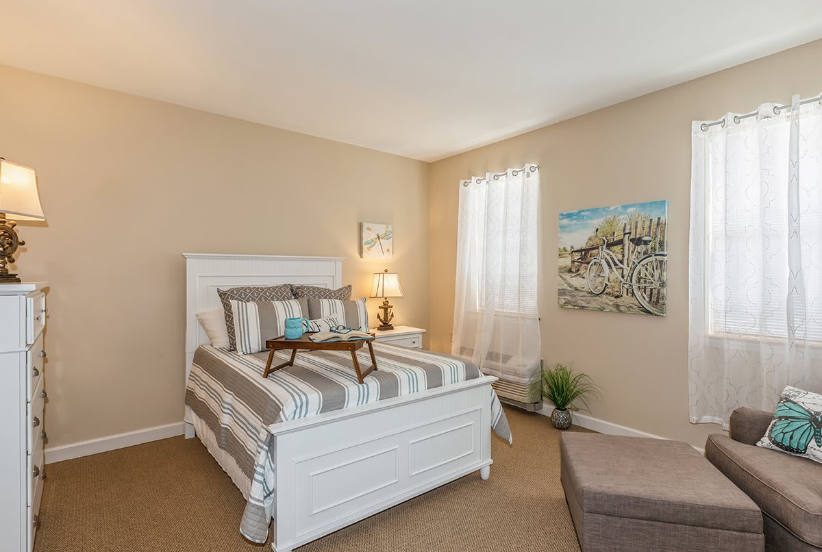 A cozy bedroom with neutral tones features a white bed with striped bedding, a decorative tray, and soft lighting.
