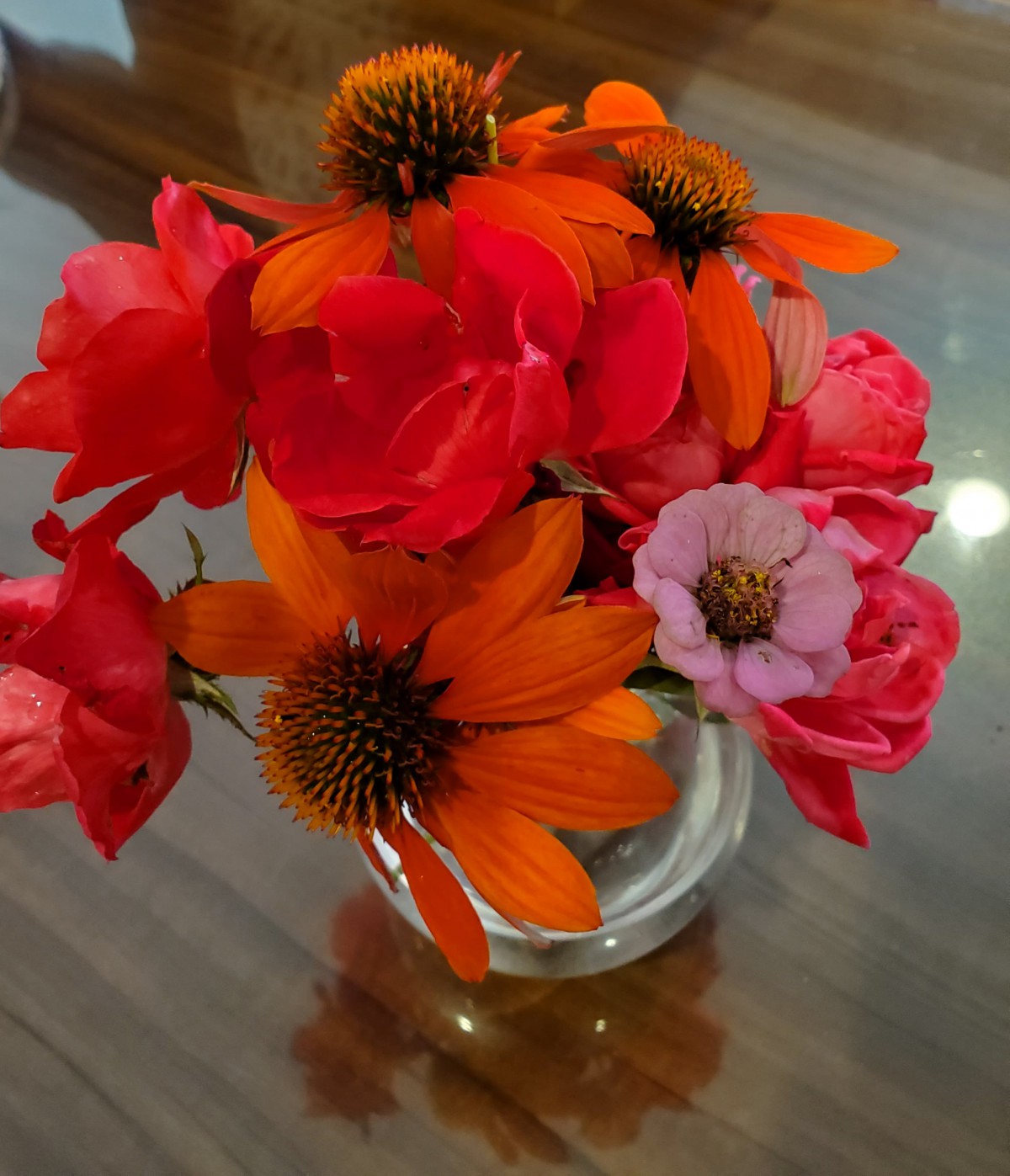 A colorful bouquet of orange and pink flowers in a glass vase on a wooden table.