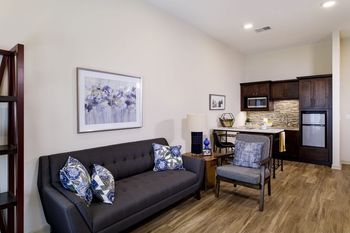 A modern living space with a sofa, chair, and kitchenette.