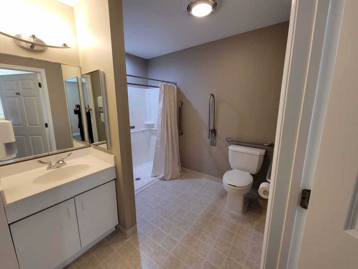 A clean and spacious bathroom with a sink, mirror, toilet, and shower area.