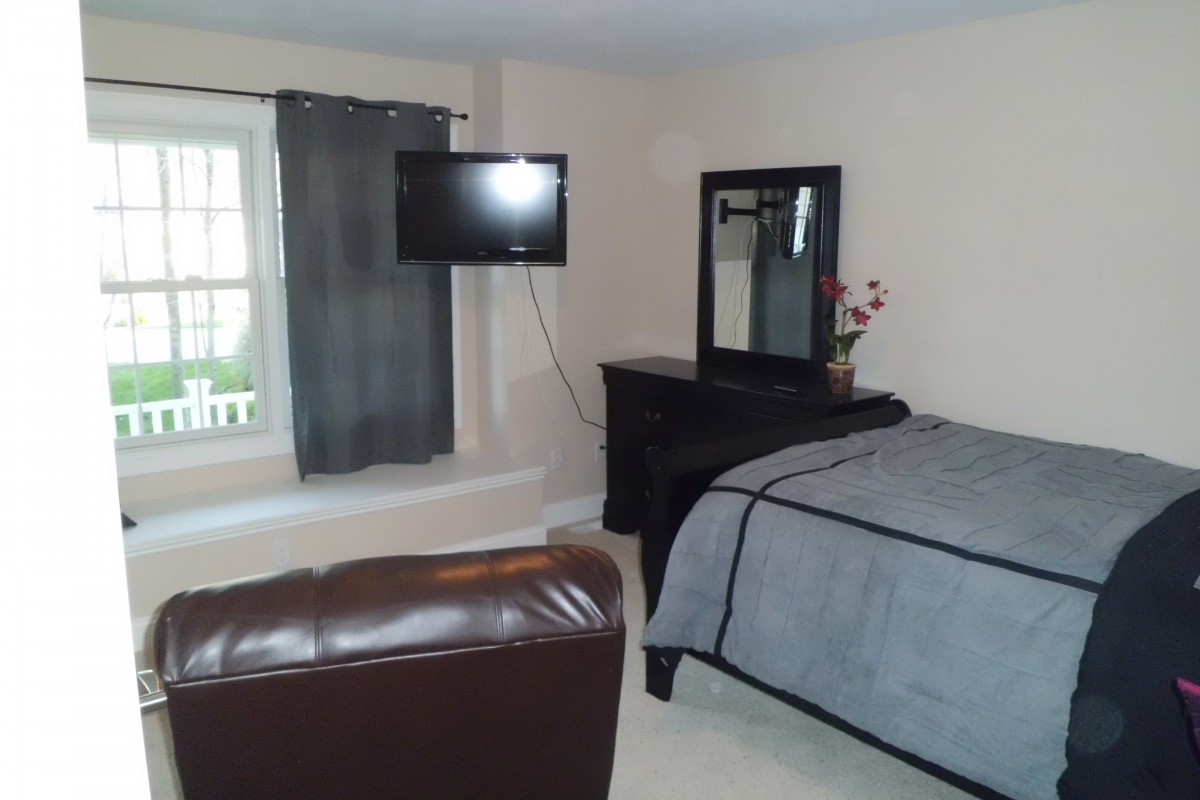A cozy bedroom featuring a bed, dresser with a mirror, and a wall-mounted television.