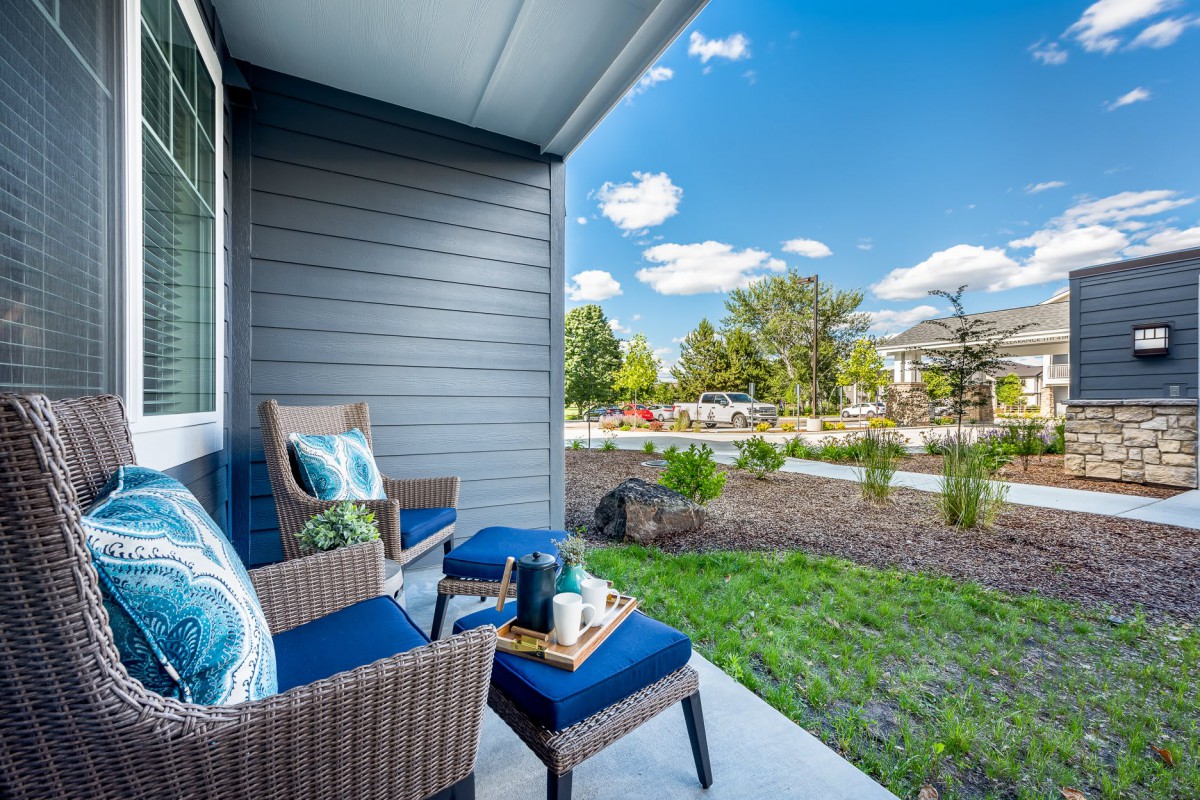 A cozy outdoor patio area with cushioned chairs and a small table, surrounded by a well-maintained garden on a sunny day.