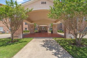 A building entrance with a covered driveway and surrounding greenery.