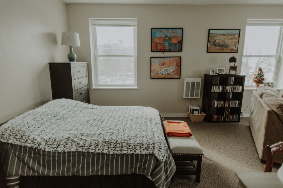 A cozy bedroom with a bed, dresser, lamp, and artwork on the walls.
