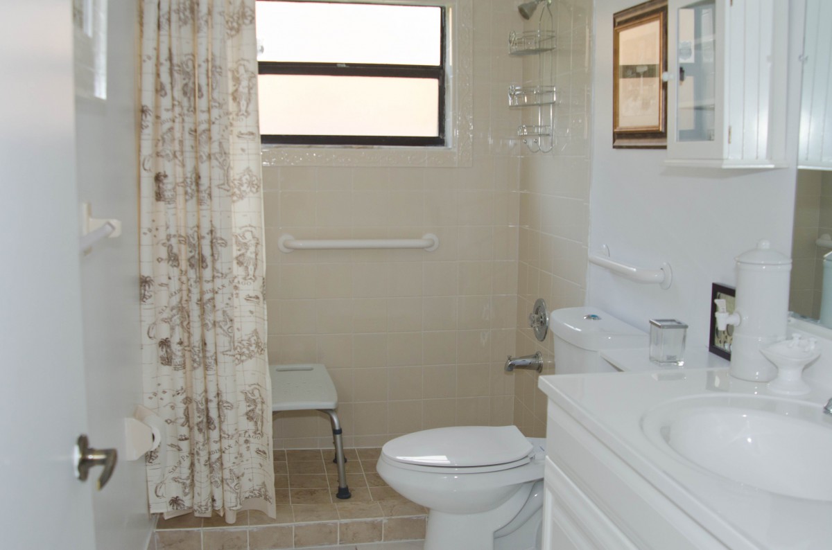 A clean bathroom featuring a toilet, shower with curtain, sink, and window.