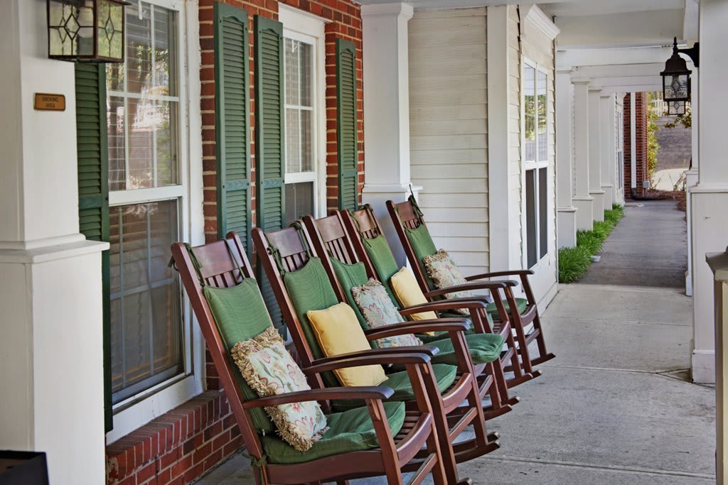 A row of rocking chairs with colorful cushions on a porch.