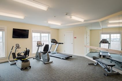 A well-lit indoor gym with various exercise equipment including treadmills and stationary bikes.