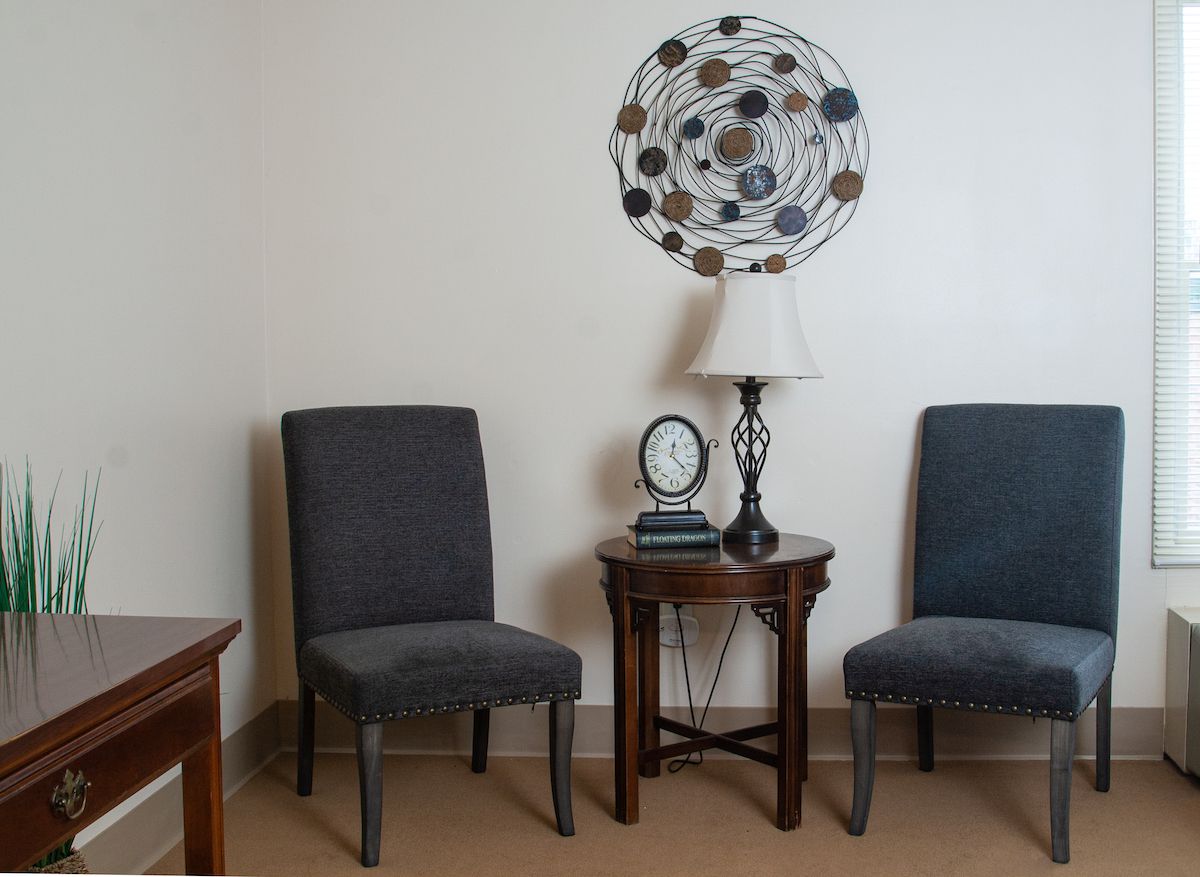 A cozy living room corner with two chairs, a side table, lamp, and decorative wall art.