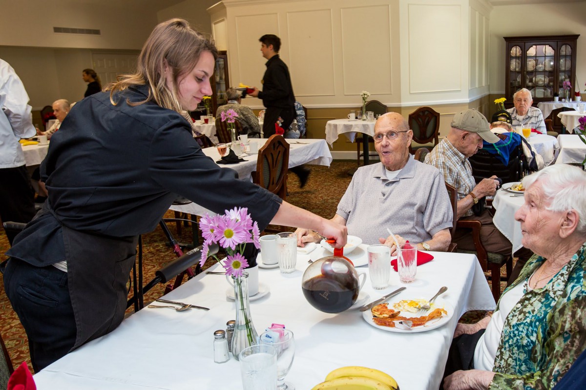A waitress serves coffee to customers seated at a restaurant table.