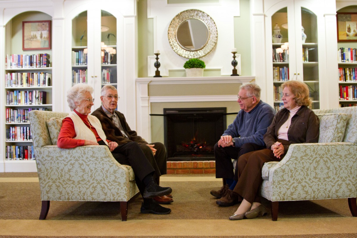 A group of seniors sitting in a living room having a conversation near the fireplace.