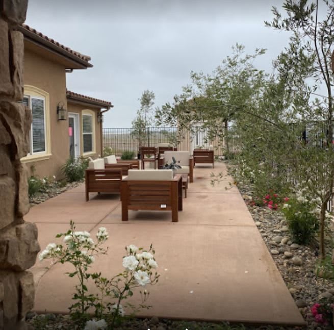A cozy patio with outdoor seating surrounded by greenery and the exterior of a house.