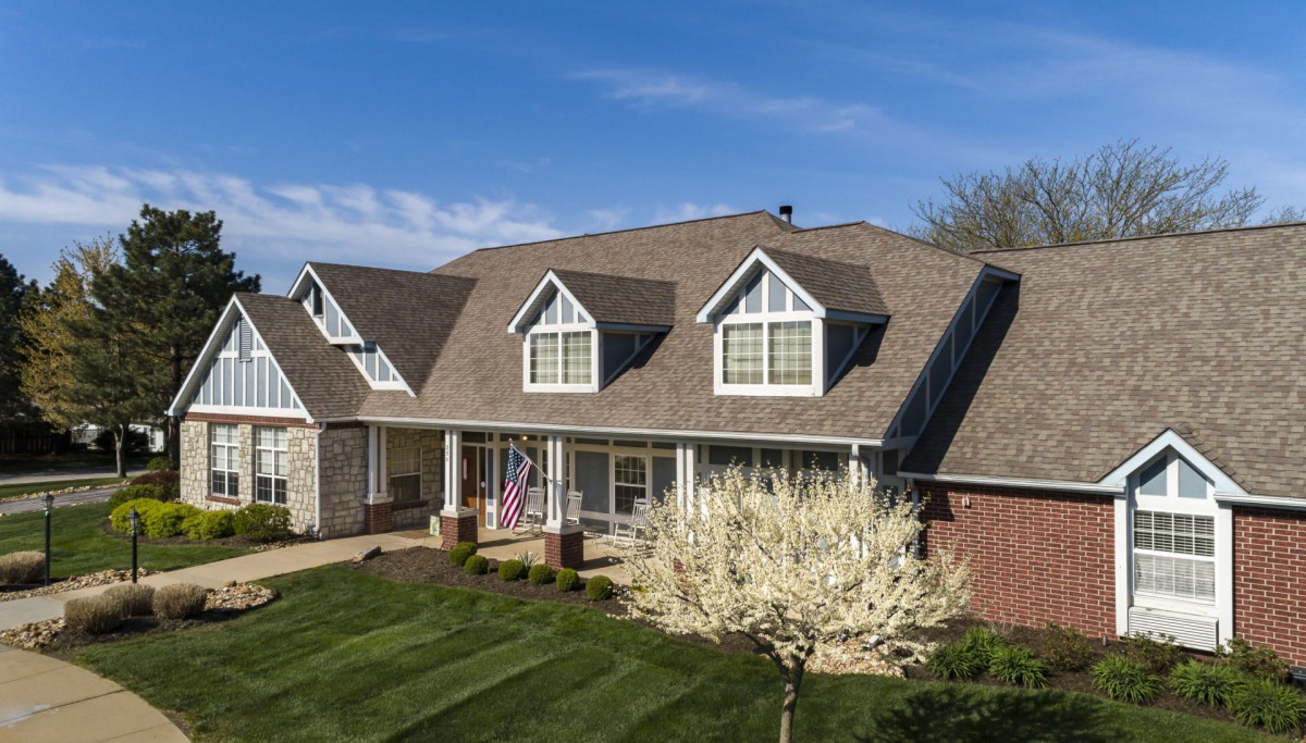 A large, suburban house with a well-maintained lawn and garden under a clear blue sky.