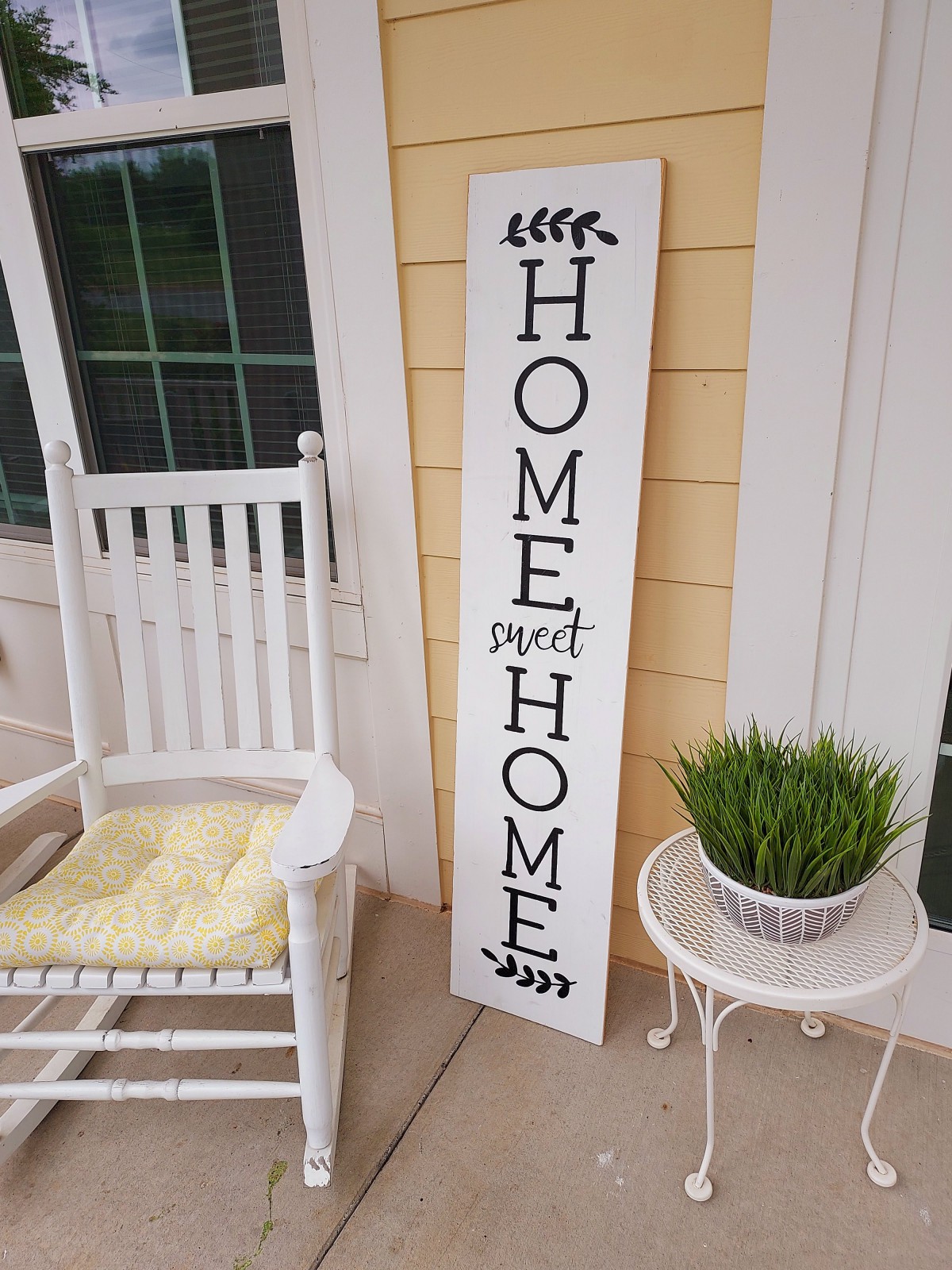 A cozy front porch with a 'Home Sweet Home' sign, a rocking chair, and a potted plant.