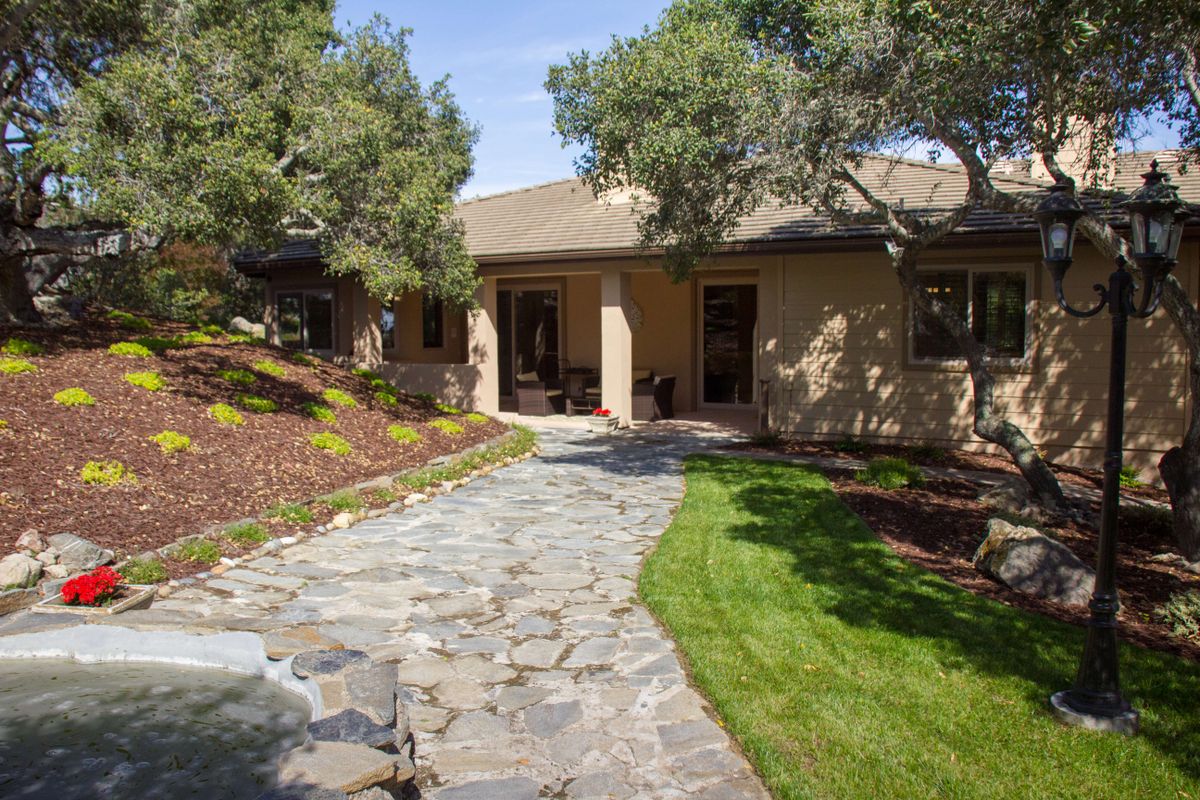 A well-landscaped front yard with a stone pathway leading to a house surrounded by trees and grass.