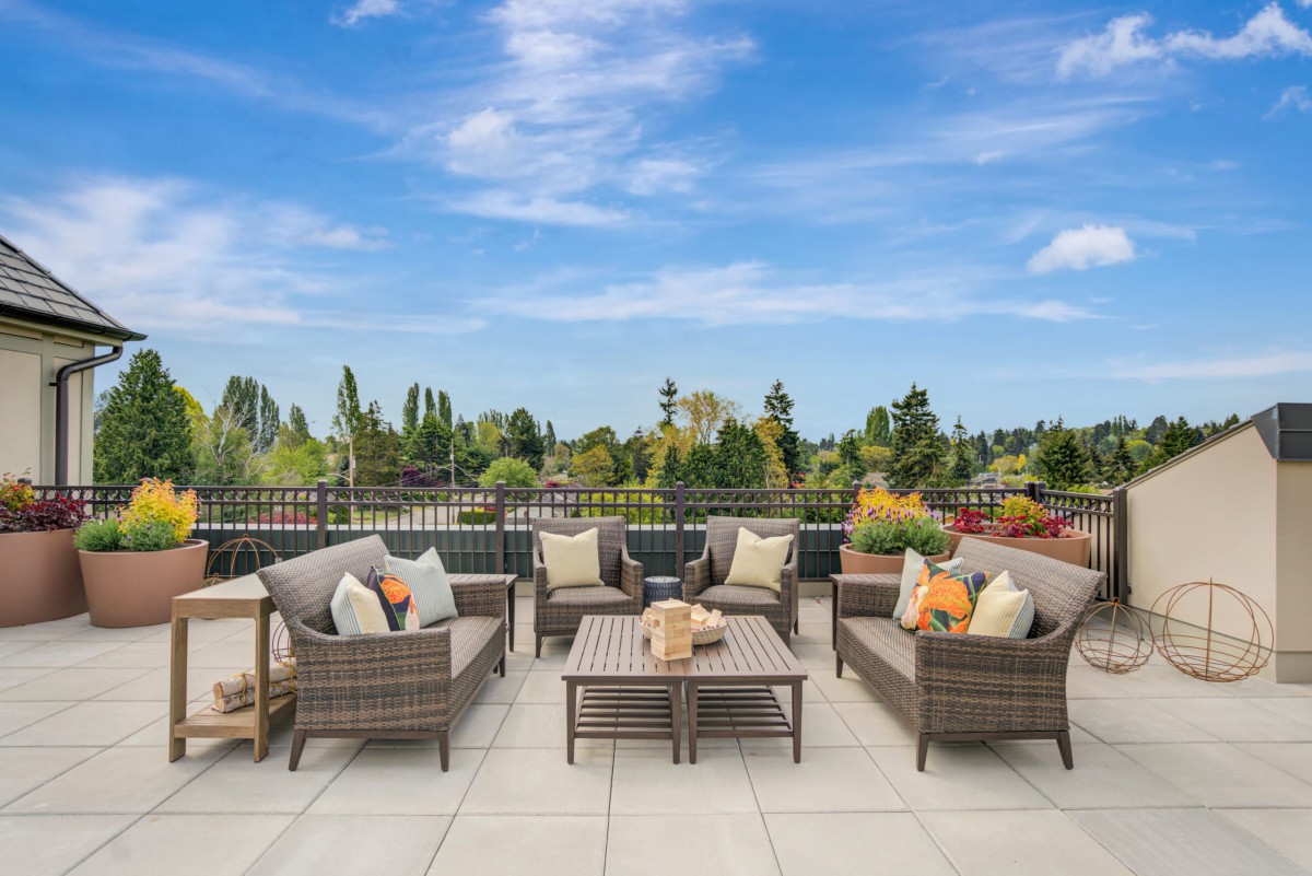 A spacious patio area featuring wicker furniture with cushions, set against a backdrop of a clear blue sky and lush greenery.