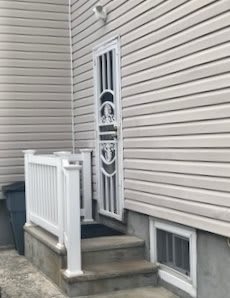 A house exterior featuring a narrow metal door with decorative elements, accessed by a small staircase with white railings.