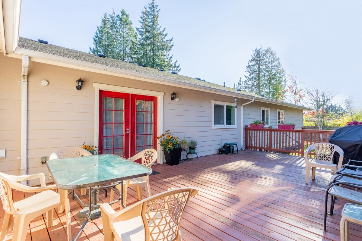 A spacious outdoor deck with a table, chairs, and red double doors leading into the house.