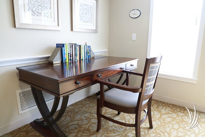 A cozy home office space with a wooden desk, books neatly arranged on top, and a comfortable upholstered chair nearby.