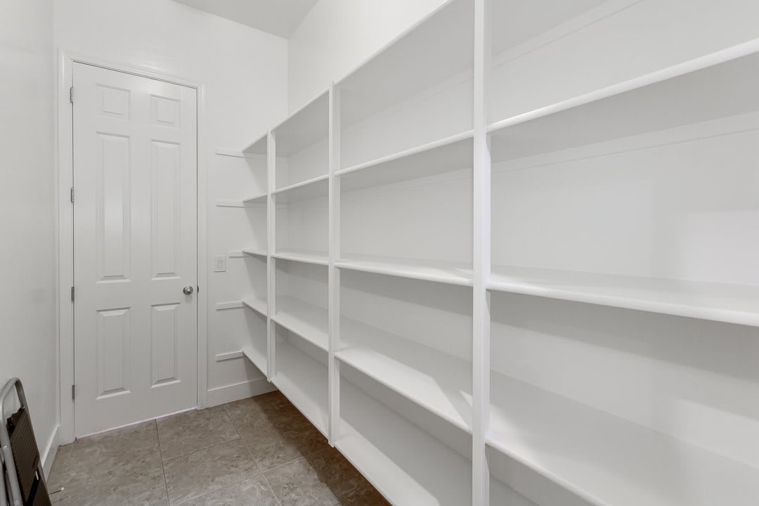 An empty pantry room with white shelves.