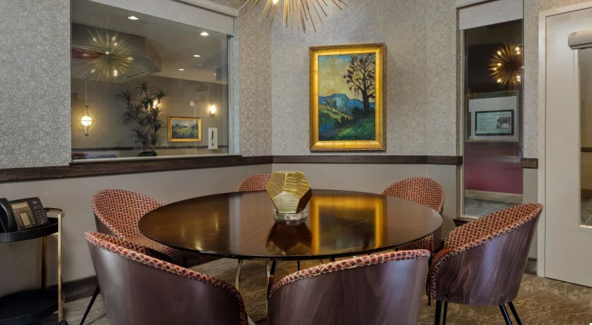 A stylish modern dining area with a round table, upholstered chairs, and a framed painting on the wall.