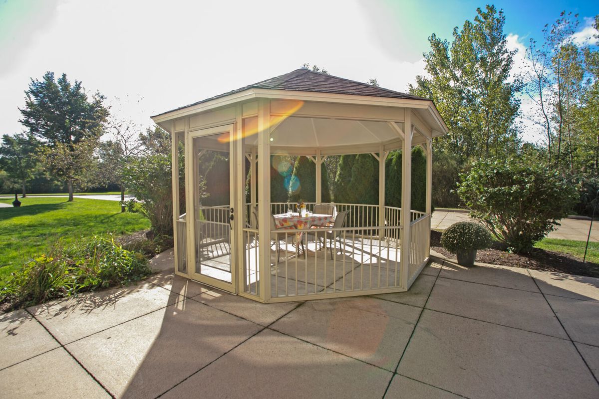 A charming wooden gazebo on a sunny patio in a garden setting.