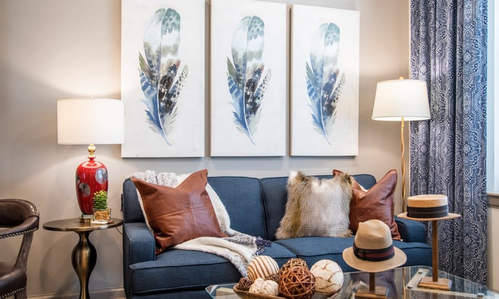 A cozy living room featuring a blue sofa with textured pillows, complemented by a set of three abstract artworks on the wall.
