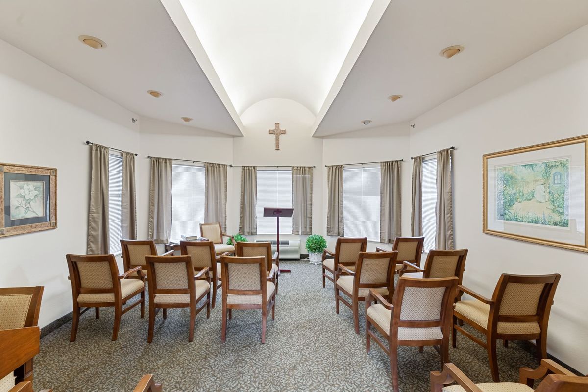 A small, serene chapel with rows of chairs facing a podium and a cross on the wall.