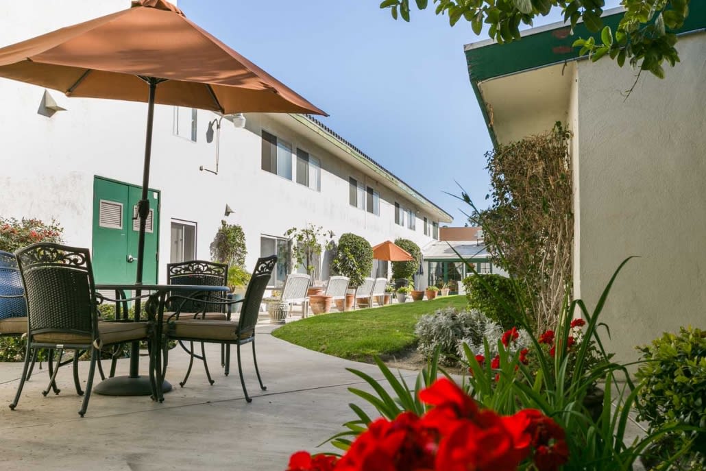 A charming courtyard with patio seating and umbrellas surrounded by well-maintained gardens.