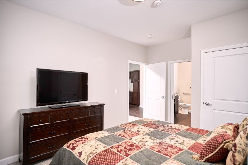 A modern bedroom featuring a TV on a dresser, with a bed covered in a colorful quilt.