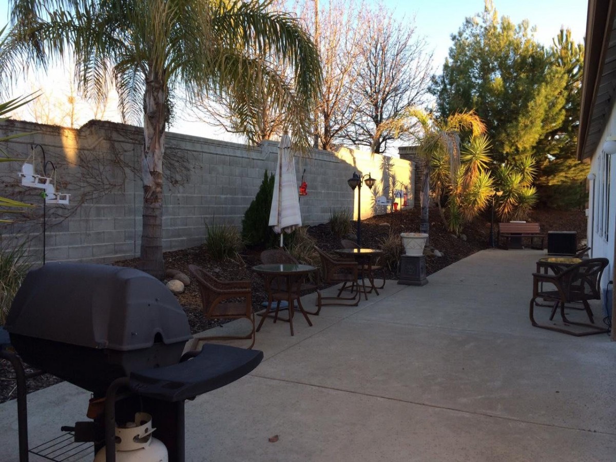 A sunny backyard patio with outdoor furniture and a grill.