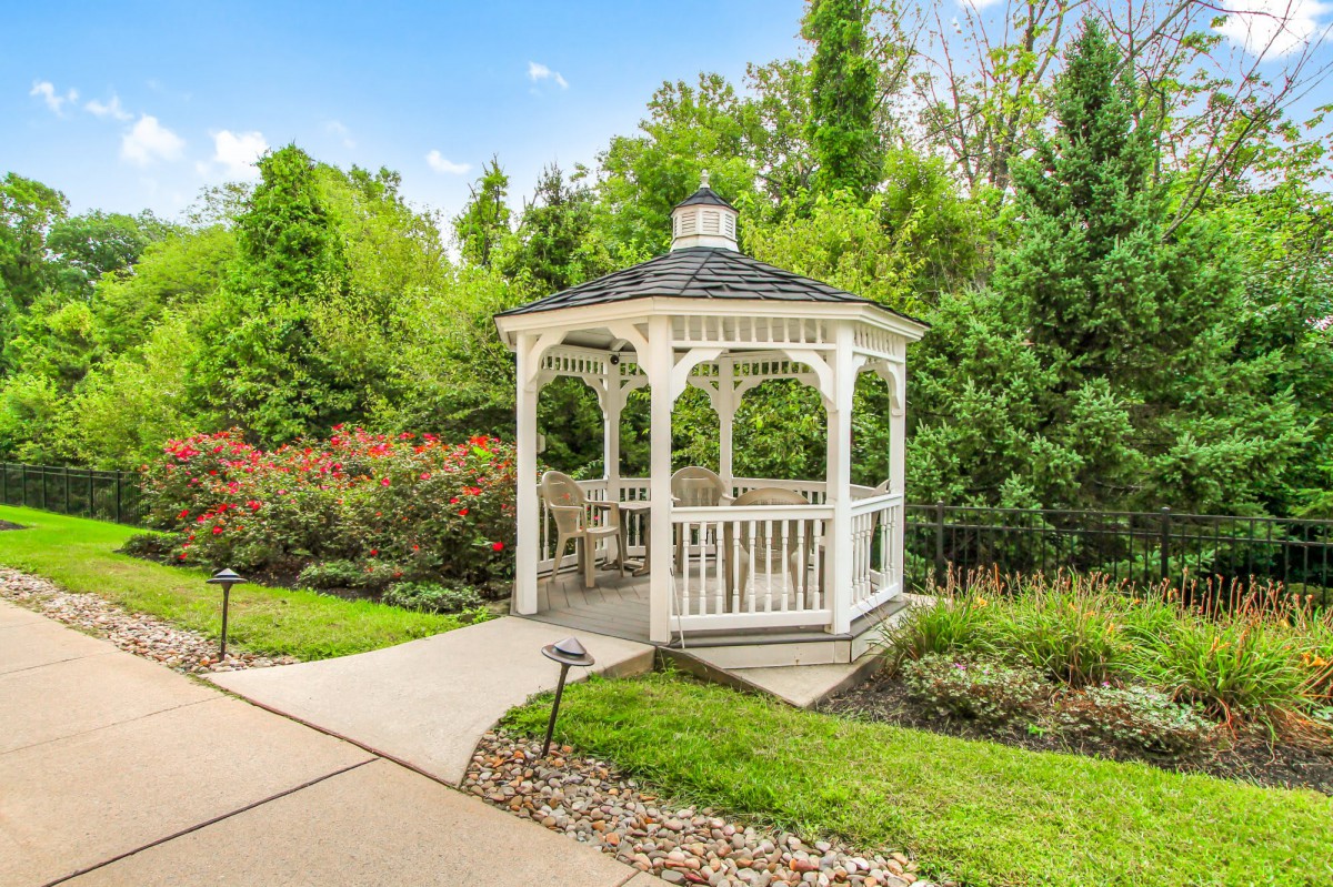 A charming white gazebo surrounded by lush greenery in a garden setting.