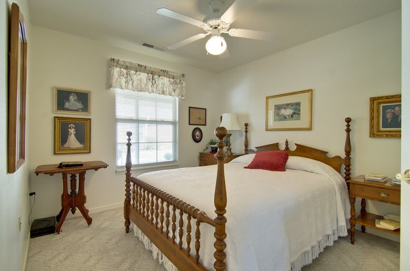 A cozy bedroom with a wooden bed, decorated with framed artwork and a ceiling fan.