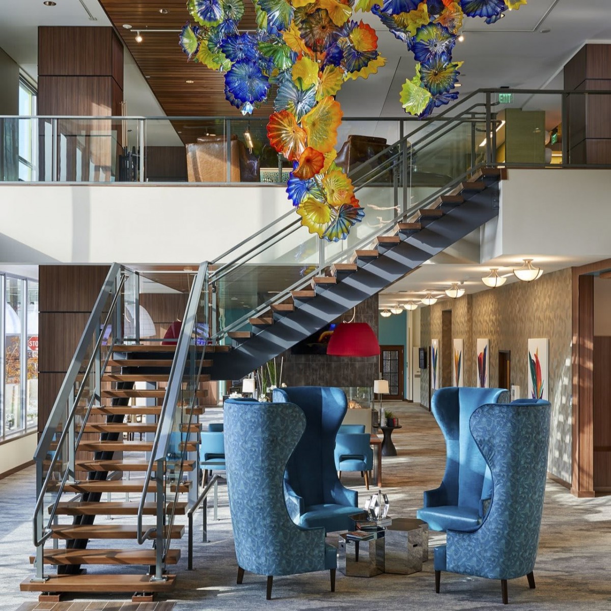 A modern lobby featuring a striking chandelier, a stylish staircase, and comfortable seating area.
