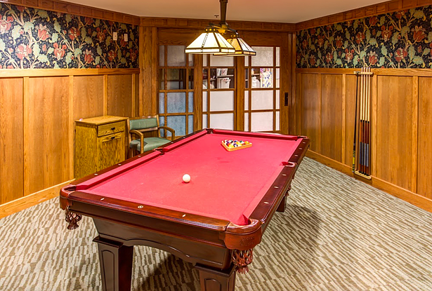 A cozy game room featuring a red-felt pool table under a decorative light fixture.
