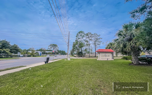 A serene view of a grassy area alongside a road, featuring trees and a small building under a clear blue sky.