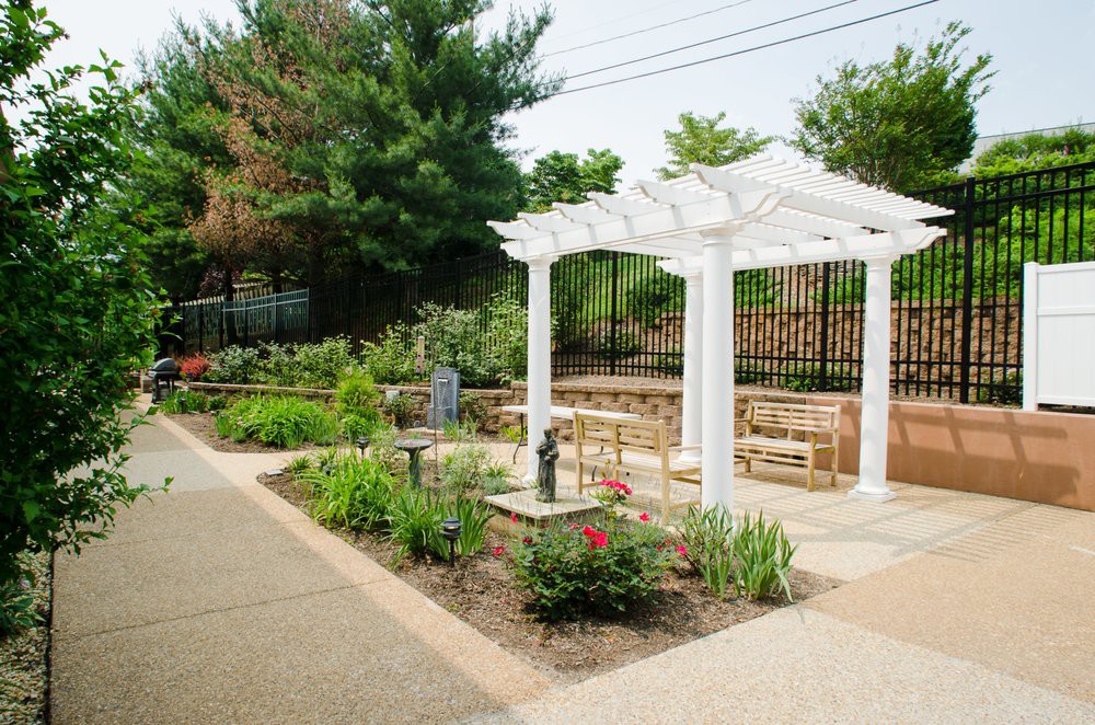 A serene garden with a white pergola and benches surrounded by lush greenery.