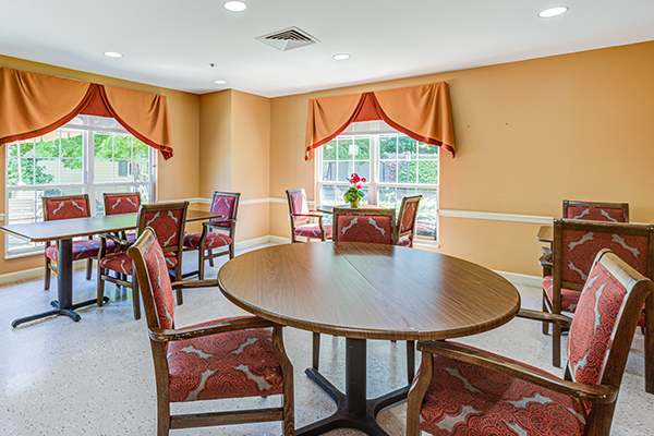 A cozy dining area with round tables, chairs, and large windows adorned with orange curtains.