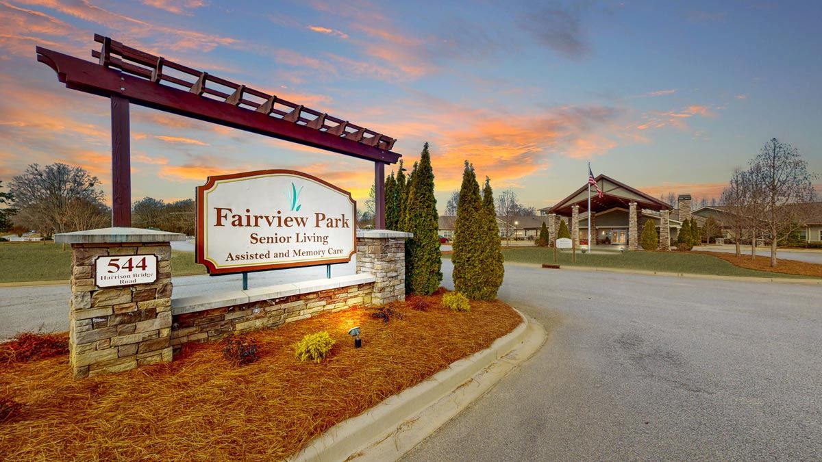 Entrance to Fairview Park Senior Living with a welcoming sign and scenic landscaping at sunset.