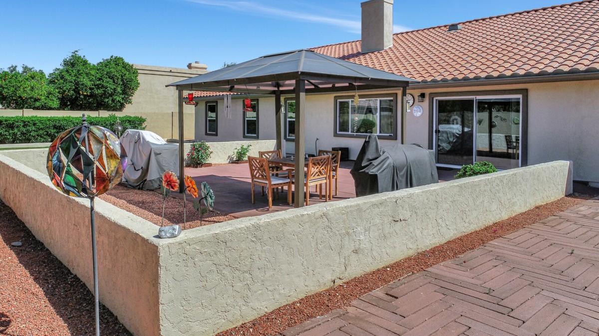 A cozy backyard patio with a canopy, table, chairs, and a grill setup for outdoor dining.