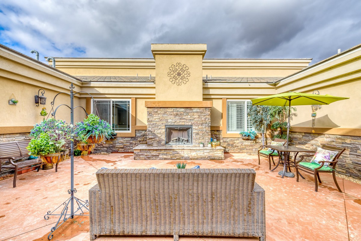 A spacious outdoor patio featuring a central fireplace, comfortable seating, and vibrant greenery under a cloudy sky.