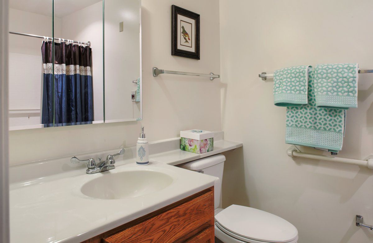 A clean and organized bathroom with a sink, toilet, mirror, and neatly arranged towels.