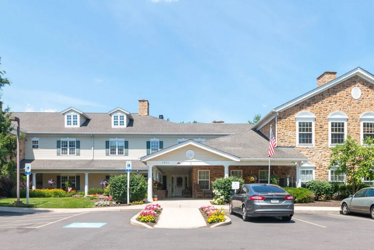 A front view of a residential building with a car parked in the driveway and flowers lining the entrance.