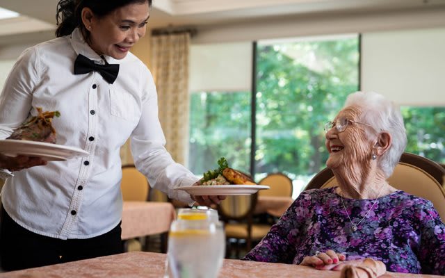 A waiter serves food to an elderly woman at a restaurant.