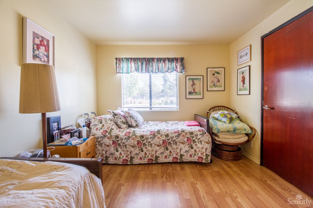 A cozy bedroom featuring a single bed with floral bedding, an armchair, and wall decorations.