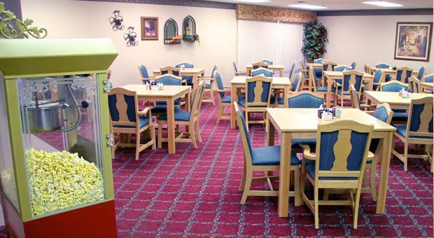An empty dining area with tables and chairs, featuring a patterned carpet and an arcade machine in the corner.