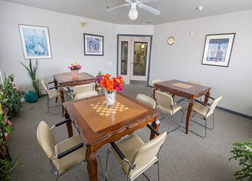 A cozy room with multiple tables featuring chess board designs, surrounded by chairs and decorated with vases of flowers.