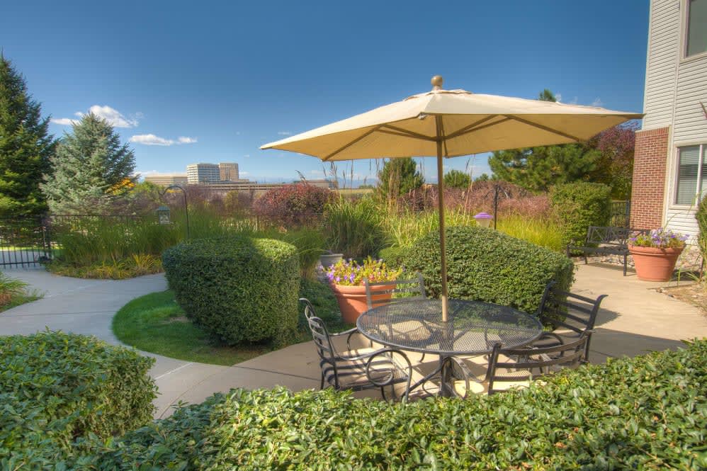 A tranquil garden patio featuring outdoor seating with an umbrella amidst lush greenery.