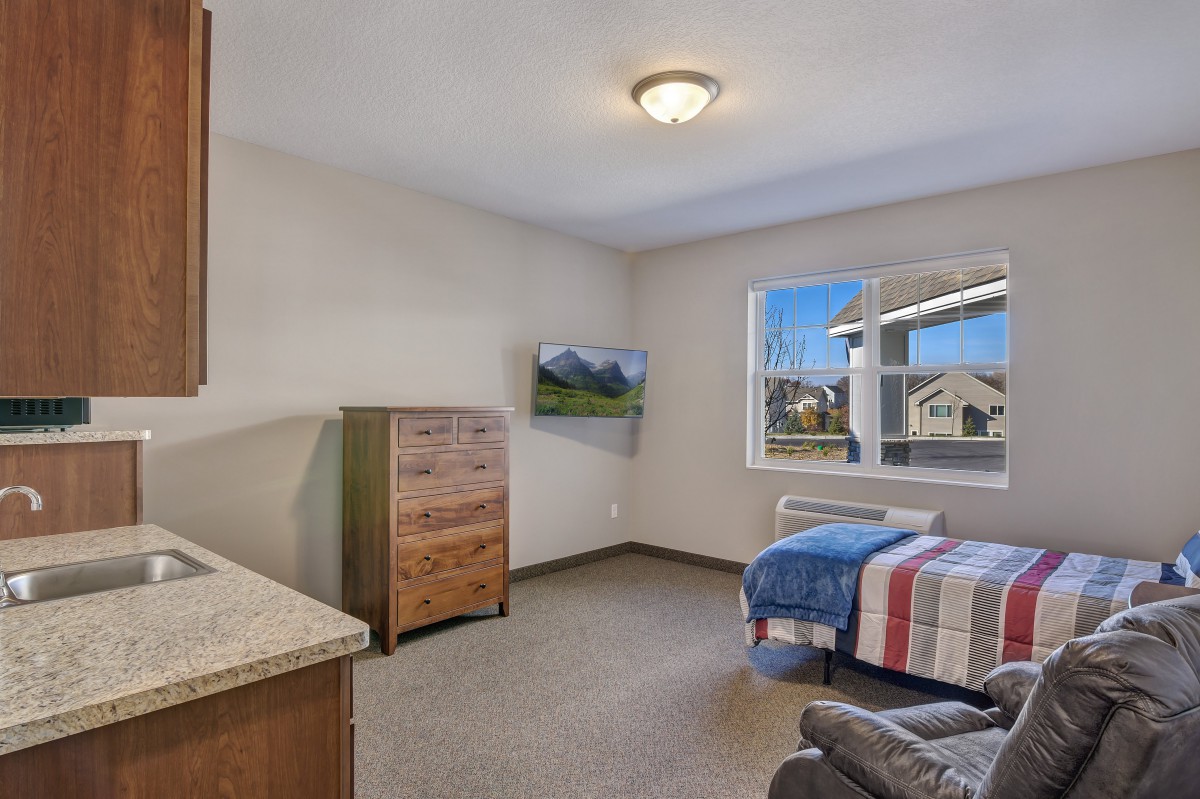 A well-lit bedroom with a single bed, dresser, and wall-mounted TV.