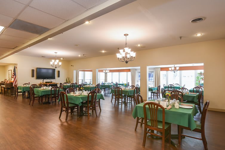 A spacious dining area with neatly arranged tables and chairs, illuminated by elegant chandeliers.