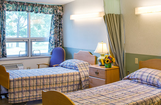 A well-lit shared hospital room featuring two beds, a nightstand with a lamp, and colorful curtains.